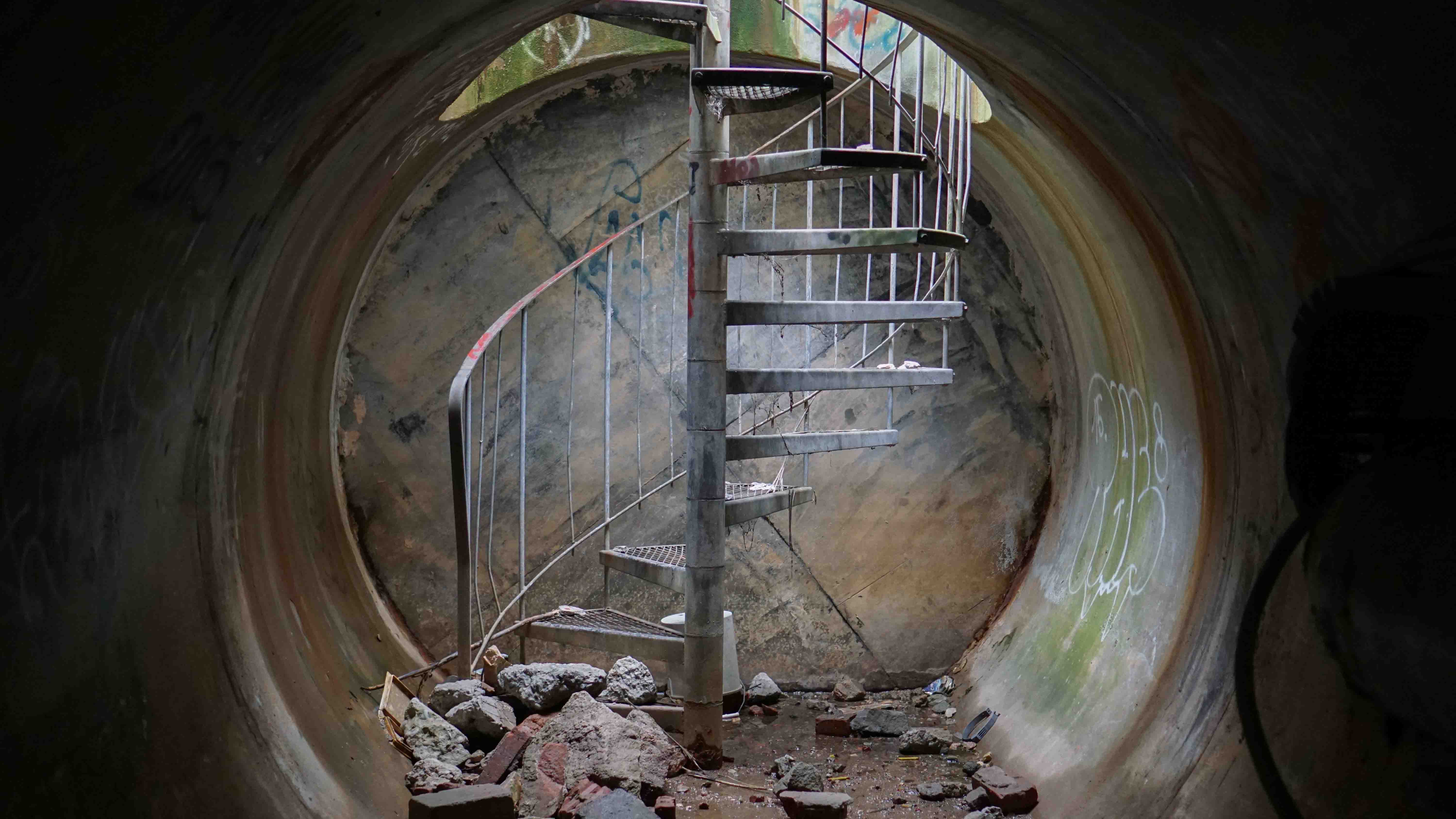 Forladt spiraltrappe i cirkulær betonåbning med graffiti